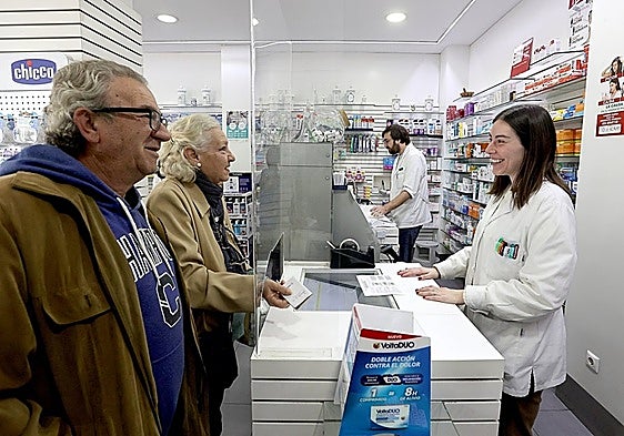 A professional attends to two customers in a pharmacy in Cordoba.