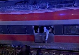 A passenger tries to climb out of a broken window of the derailed Iryo train.
