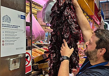 A worker at the Atarazanas market in Malaga hanging his products next to one of the city council's signs.