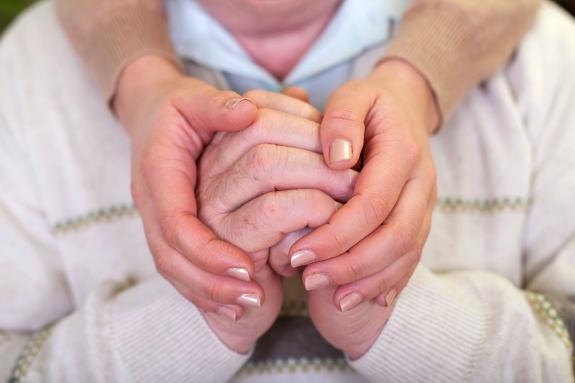 A carer holds an elderly dementia sufferer's hands.