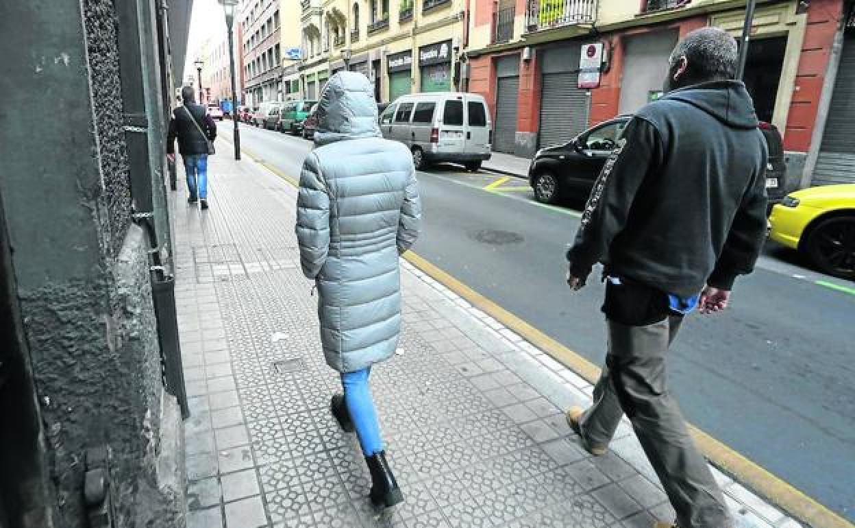 Una mujer amenazada camina precedida por uno de sus guardaespaldas y seguida por el otro escolta. 