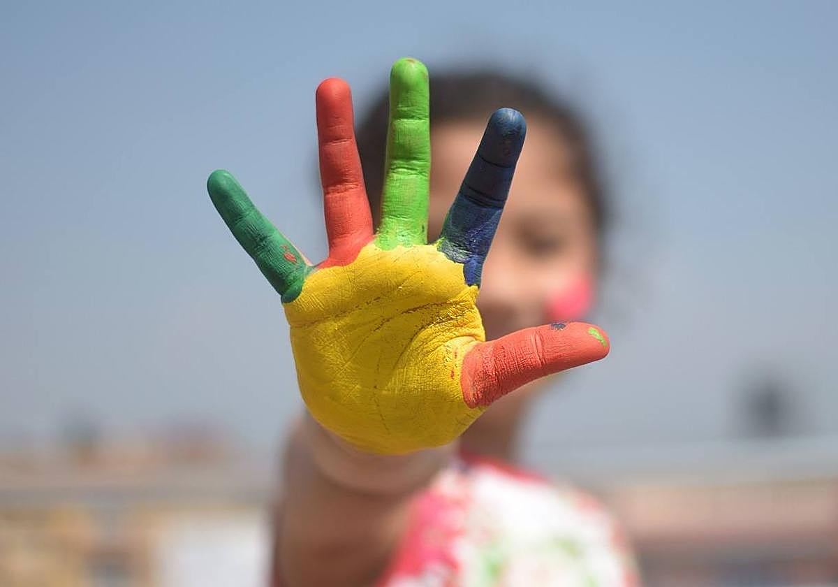 Una niña con la mano pintada de colores.