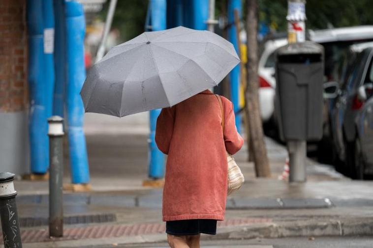 Una mujer pasea con el paraguas por la calle.