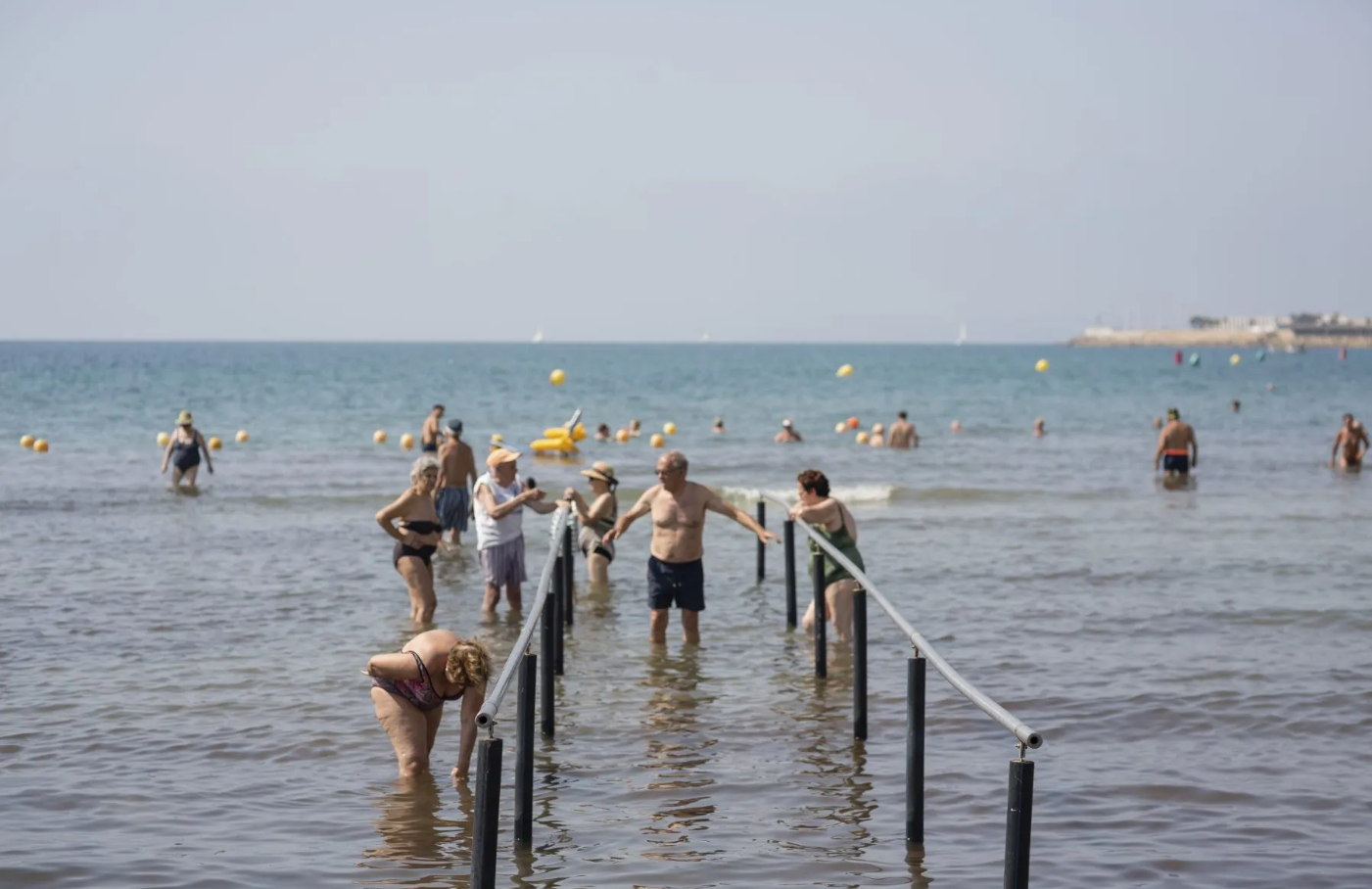 Varias personas utilizan las barandillas para entrar o salir del agua sin peligro de tropiezos.