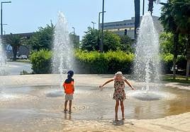 Unos niños se refrescan en una fuente.