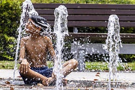 Un niño se refresca en una fuente.