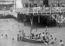 Varios bañistas disfrutan de las aguas del Postiguet con un balneario de fondo.
