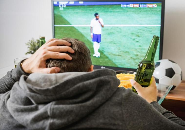 Un hombre ve un partido de fútbol por la televisión.
