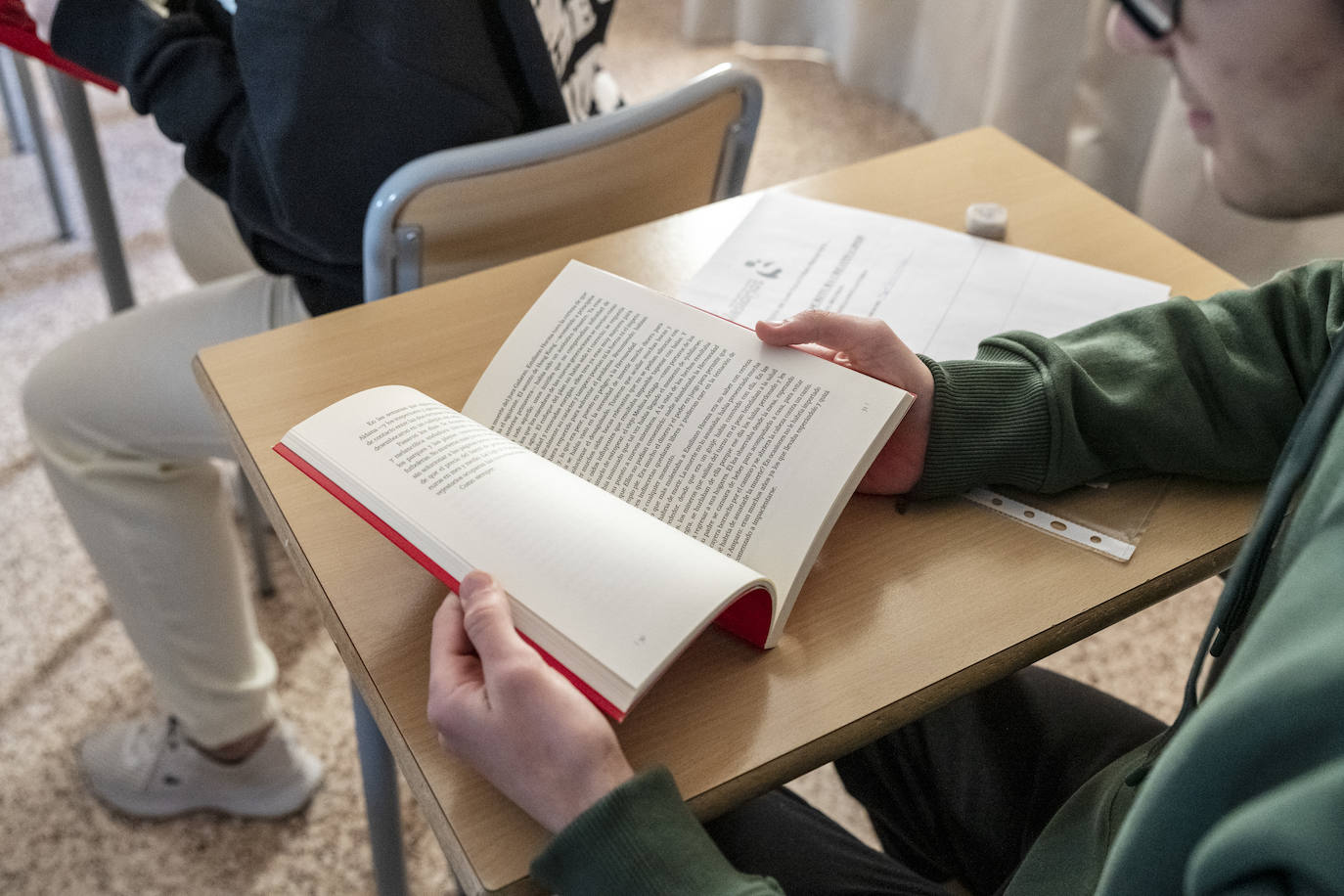 Un alumno pasa las hojas de un libro en clase.