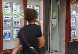 Una mujer pasa frente a una inmobiliaria con anuncios de pisos en alquiler.