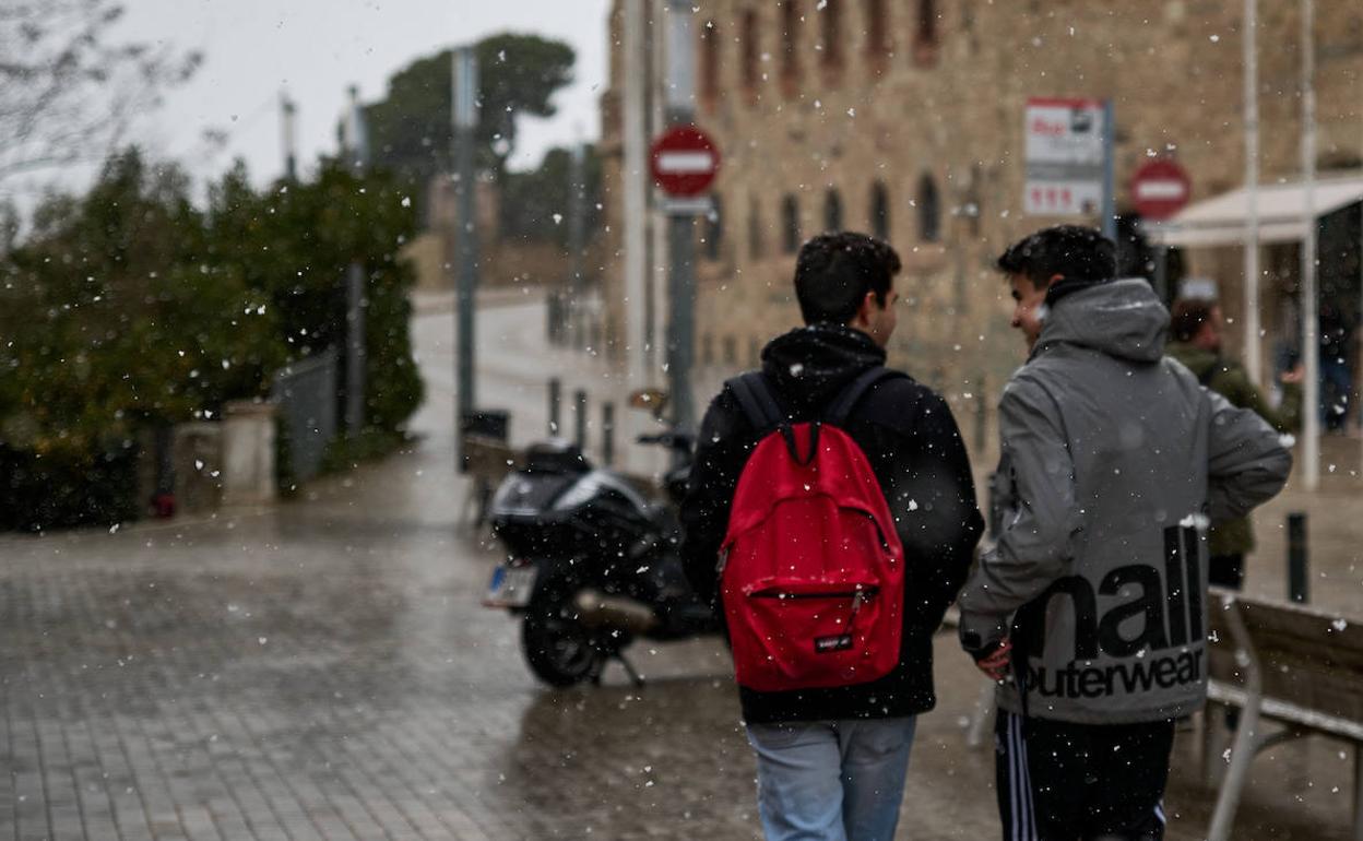 Dos escolares pasean mientras cae nieve ligera