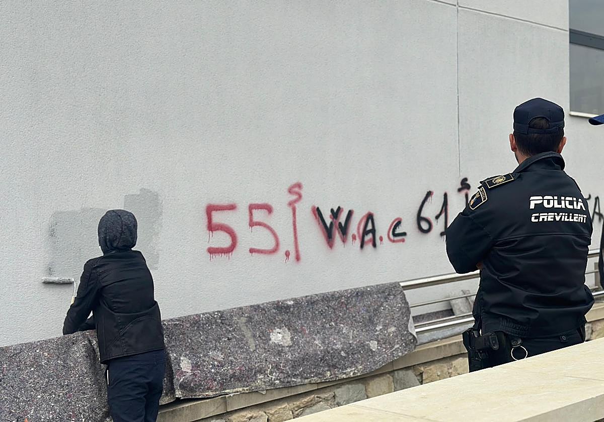 Uno de los menores limpia su grafiti ante la supervisión de un agente.