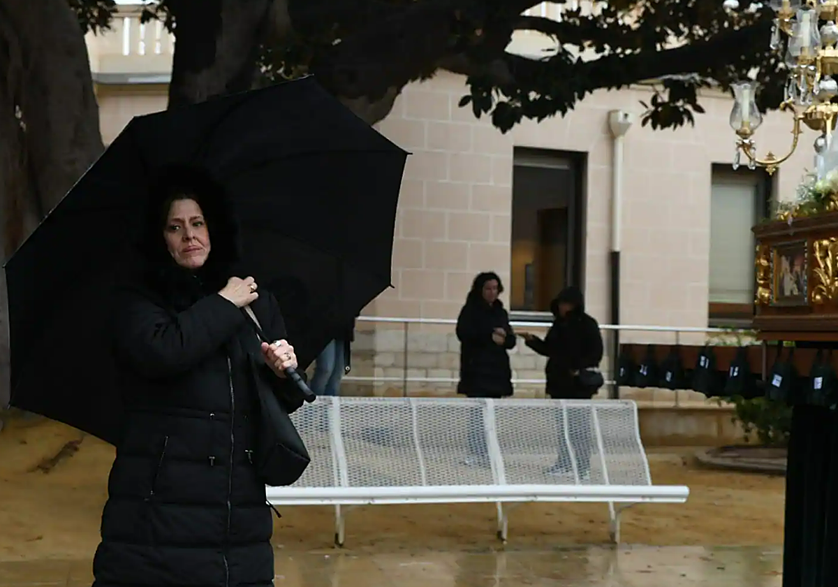 Una mujer sostiene un paraguas ante el paso de la procesión cancelada este lunes en Alicante.