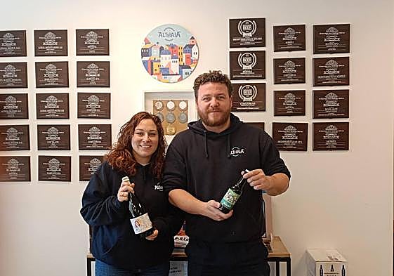 Los fundadores, Jorge y Mayte posan con cervezas delante de la pared que exhibe los premios conseguidos.