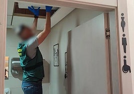 Un guardia civil inspecciona el techo del aseo de mujeres donde el detenido escondía una cámara espía.