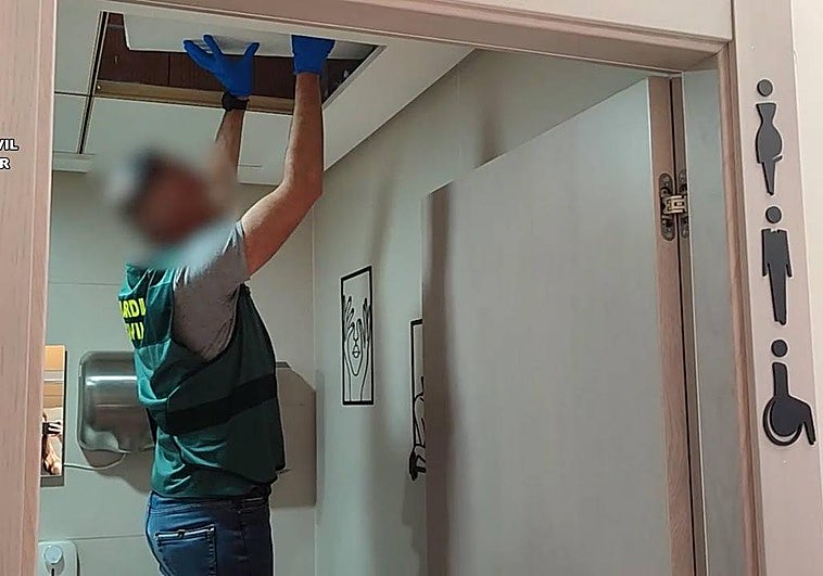 Un guardia civil inspecciona el techo del aseo de mujeres donde el detenido escondía una cámara espía.