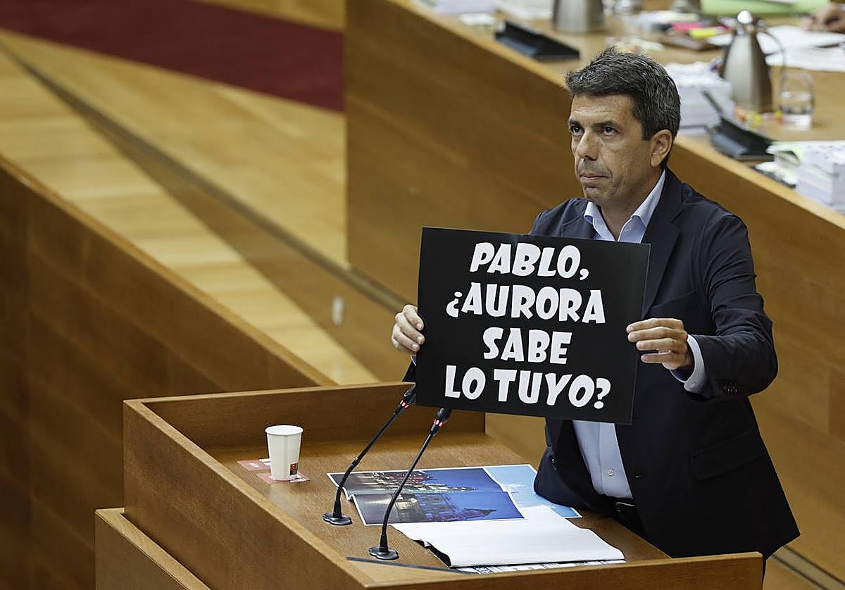 Mazón, en la tribuna, muestra uno de los carteles que en los últimos días han proliferado en Elche.
