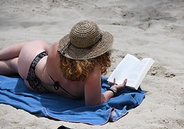 Una mujer lee un libro en la playa al sol en Alicante.