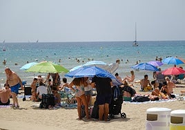 Varias personas se apelotonan bajo una sombrilla en la playa del Postiguet de Alicante.