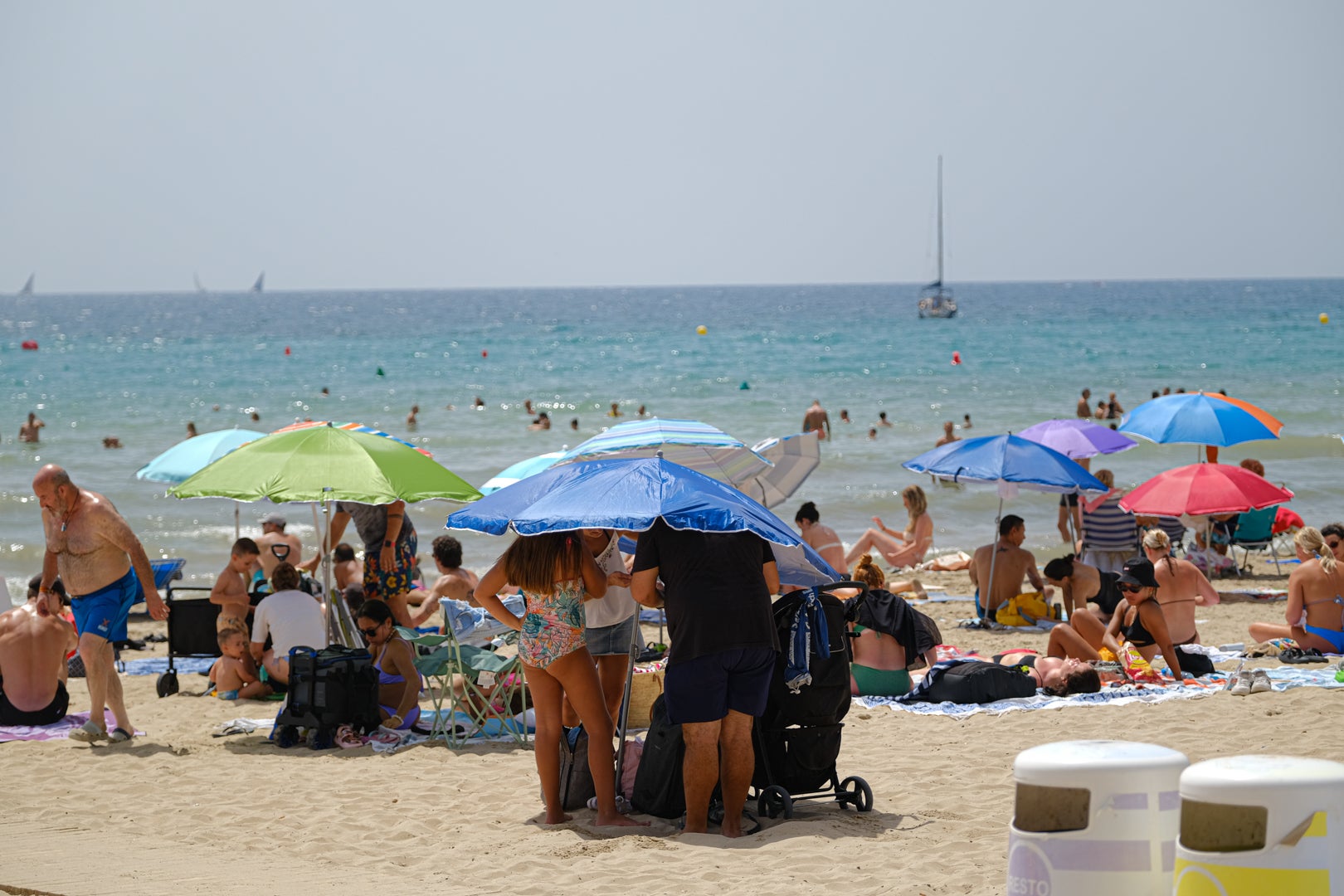 Varias personas se apelotonan bajo una sombrilla en la playa del Postiguet de Alicante.