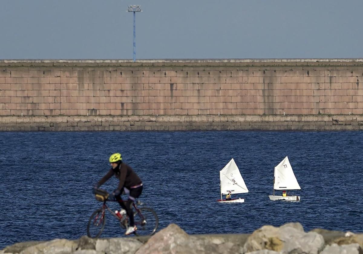 Un ciclista y unos barcos a vela navegando.