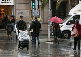 Viandantes pasean bajo la lluvia por Alicante.