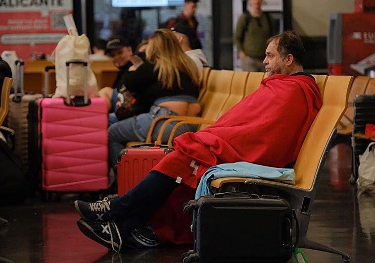 Un hombre aguarda en la estación de tren de Alicante con una manta proporcionada por la Cruz Roja.