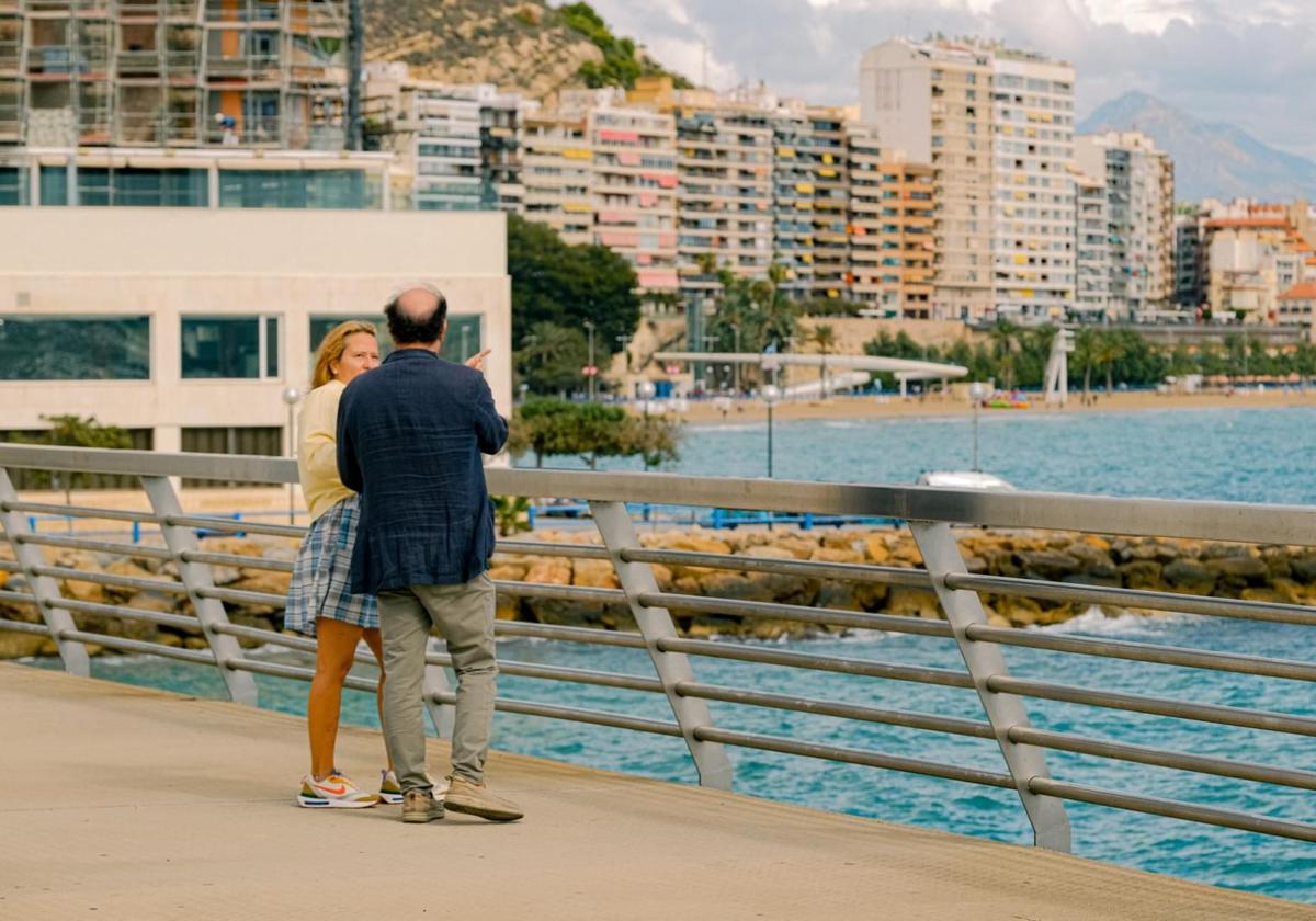 Una pareja de turistas, en la pasarela del puerto, detrás del Spa Porta Maris, miran la playa del Postiguet.