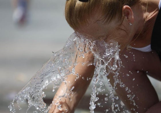 Una mujer se refresca la cara en una fuente.
