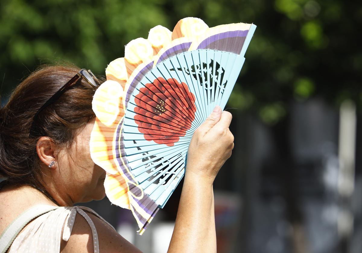 Una persona se protege del calor con un abanico.