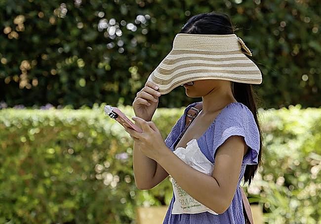 Una turista se tapa con un sombrero la cara para resguardarse del sol.