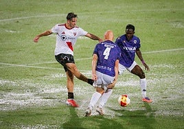 Rentero y Ben Hamed tratan de interceptar un pase de un jugador sevillista con el terreno completamente encharcado por la lluvia.